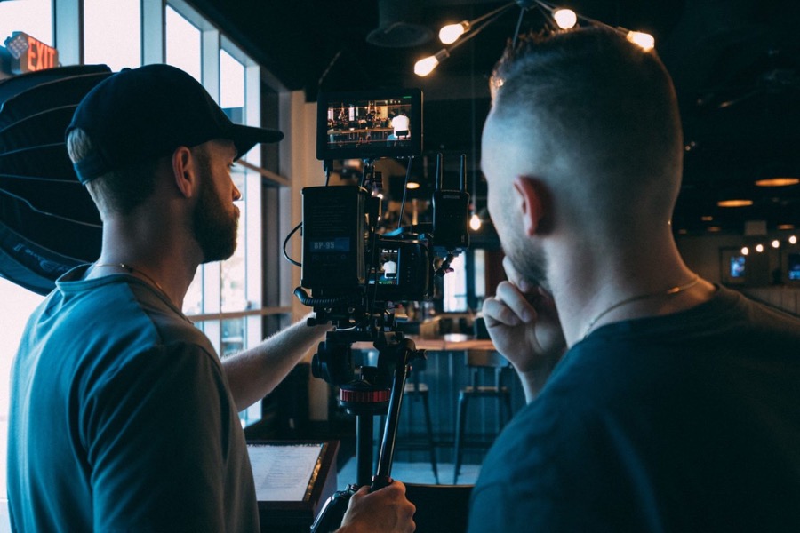 Zwei Männer filmen mit einer professionellen Videokamera in einem Raum mit dunklen Möbeln und Lichtern.