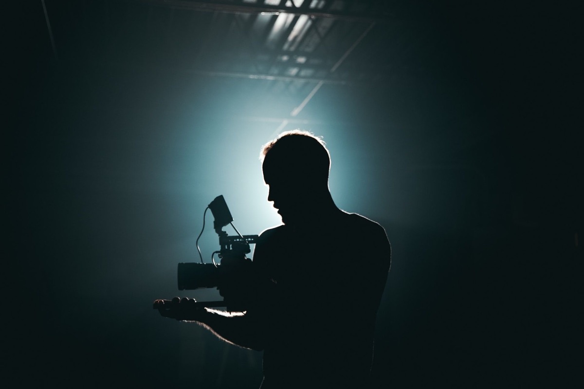 Silhouette eines Mannes, der eine Kamera vor einem hellen Scheinwerferlicht hält.